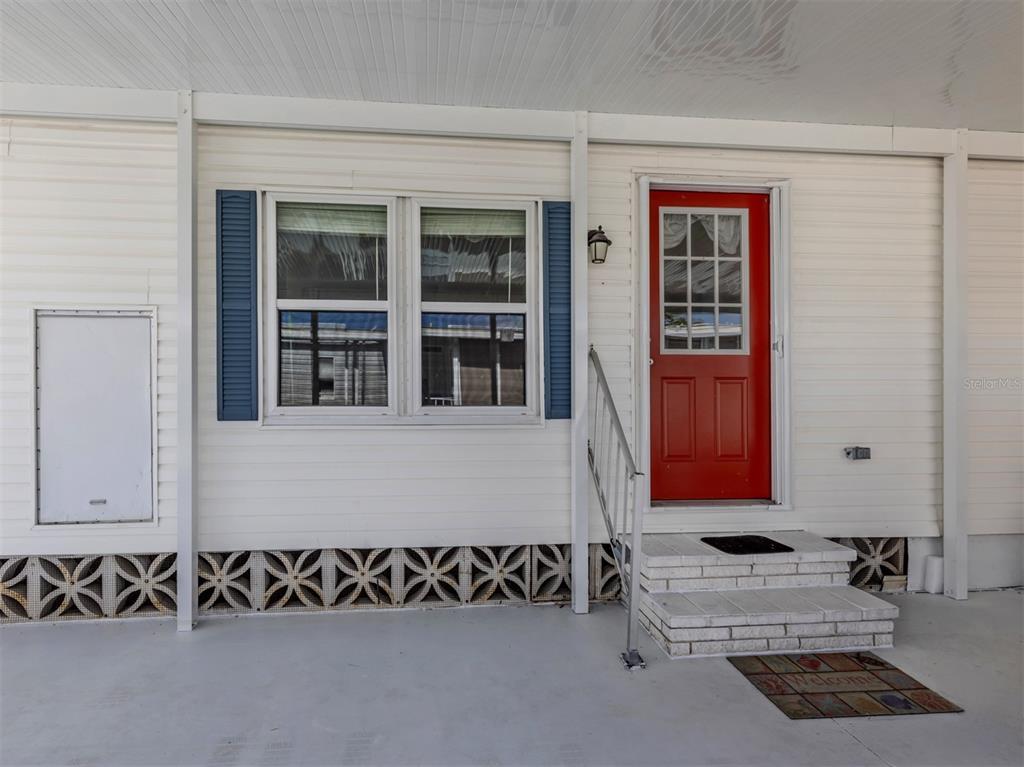 The exterior of a mobile home features white siding, blue shutters, and a red door — 98 LAKEVIEW DRIVE, NORTH PORT, FL