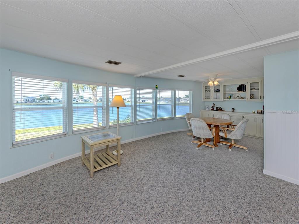 A light blue dining room features carpeted floors, large windows overlooking water, and built-in cabinetry — 98 LAKEVIEW DRIVE, NORTH PORT, FL