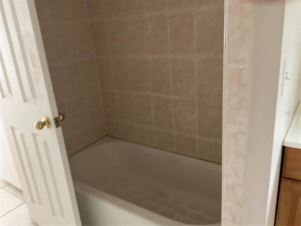 A white bathtub is surrounded by tan square wall tiles in a small bathroom — 2121 LAKEVIEW DRIVE, SEBRING, FL