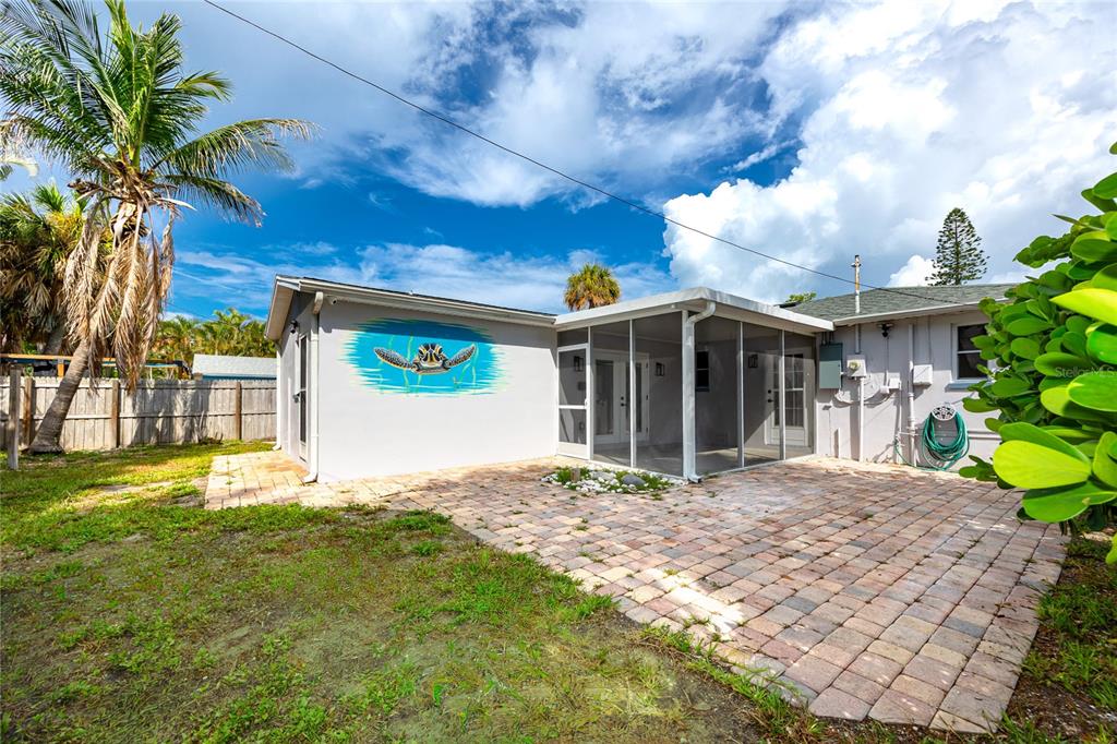 A backyard features a paved patio, a screened-in porch, and a turtle mural on the wall — 504 79TH AVENUE, ST PETERSBURG, FL