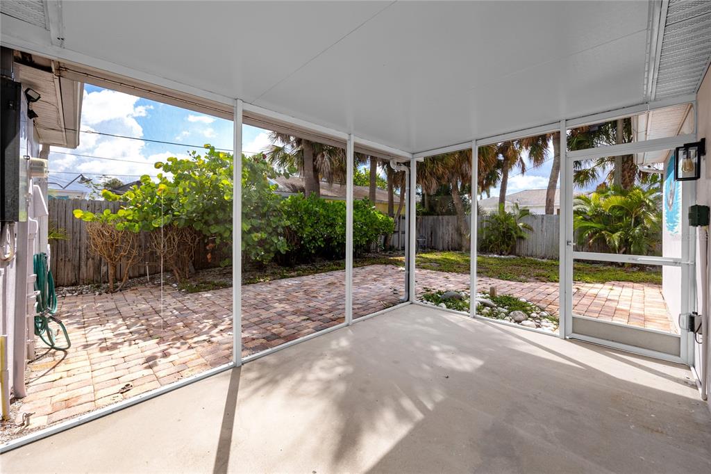 A screened-in patio with a concrete floor overlooks a brick-paved backyard with palm trees — 504 79TH AVENUE, ST PETERSBURG, FL