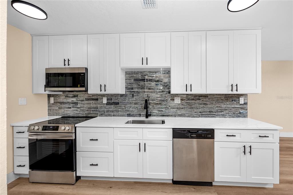A kitchen features white cabinets, stainless steel appliances, and a gray tiled backsplash — 504 79TH AVENUE, ST PETERSBURG, FL