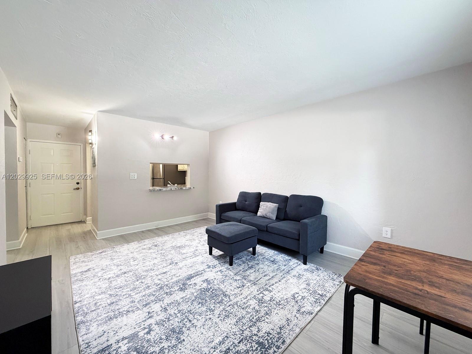 A living room features light wood-look flooring, a gray sofa with ottoman, and a rug — 8601 SW 68 CT # 5, Pinecrest FL 33156, PINECREST, FL