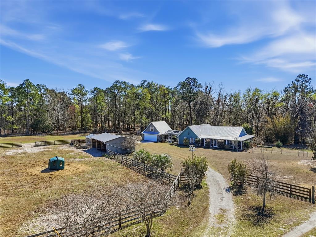 A gravel driveway leads to a green house with a metal roof behind a fence — 27471 NW 173RD TERRACE, ALACHUA, FL