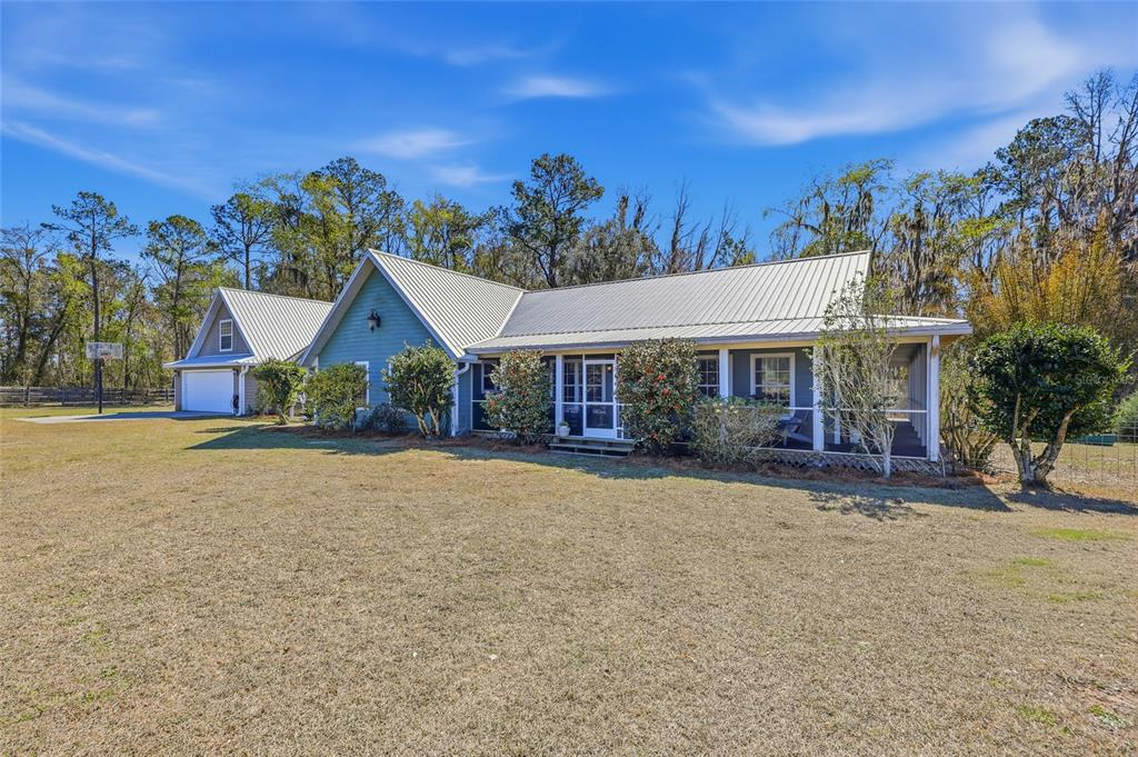 A green house with a metal roof and an attached garage sits on a lawn — 27471 NW 173RD TERRACE, ALACHUA, FL
