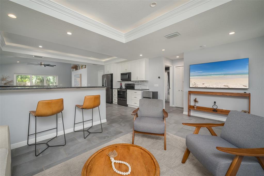 A living room with gray tile floors, two armchairs, and an open kitchen with bar stools — 1039 23RD STREET, SARASOTA, FL