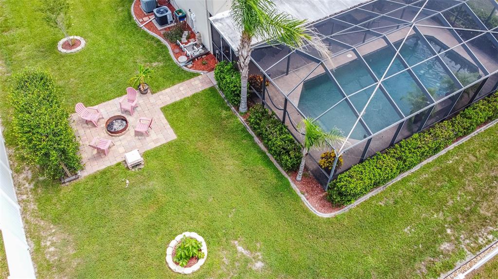 An aerial view shows a backyard with a screened pool, patio, fire pit, and landscaping — 10446 AVILA STREET, SPRING HILL, FL
