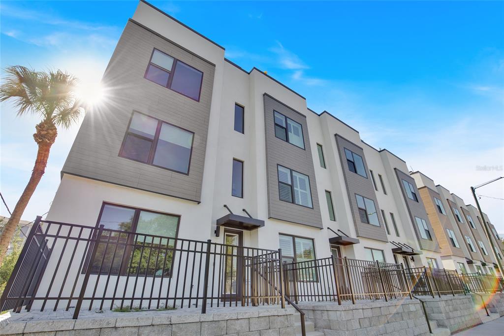 A low-angle view of a modern multi-story townhouse complex with a black metal fence — 2506 W CLEVELAND STREET UNIT 9, TAMPA, FL