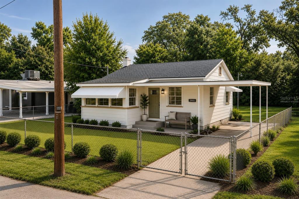 A white cottage with a covered carport and a chain-link fence in the front yard — 3905 N CLEARFIELD AVE, TAMPA, FL