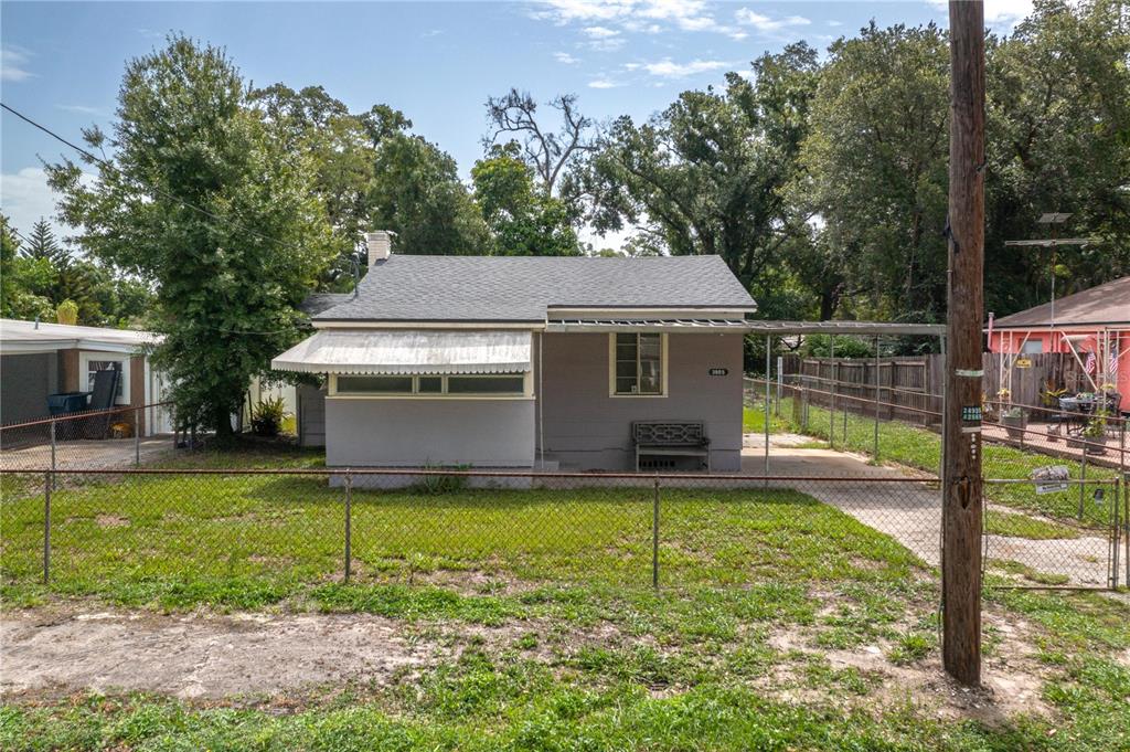 A small, gray, single-story house with a metal carport and a chain-link front fence — 3905 N CLEARFIELD AVE, TAMPA, FL