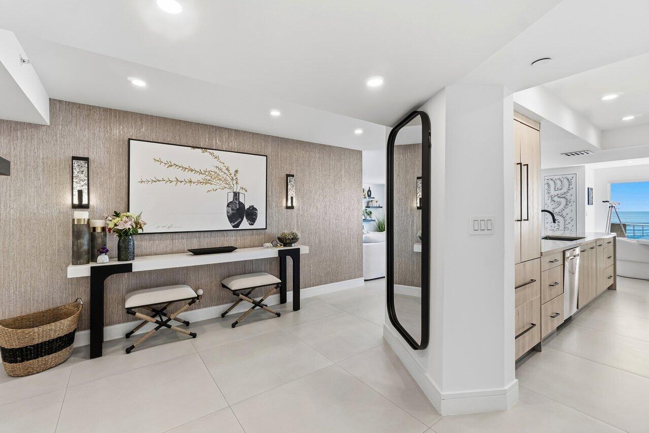 A modern entryway features a console table, two stools, wall art, and a full-length mirror — 4001 N Ocean Boulevard # 907, Boca Raton FL 33431, BOCA RATON, FL