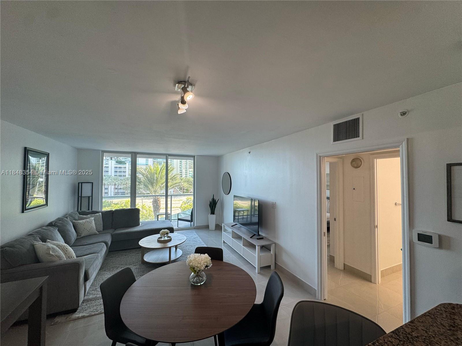 A living and dining area features a gray sectional sofa, round table, and balcony view — 1155 Brickell Bay Dr # 307, Miami FL 33131, MIAMI, FL
