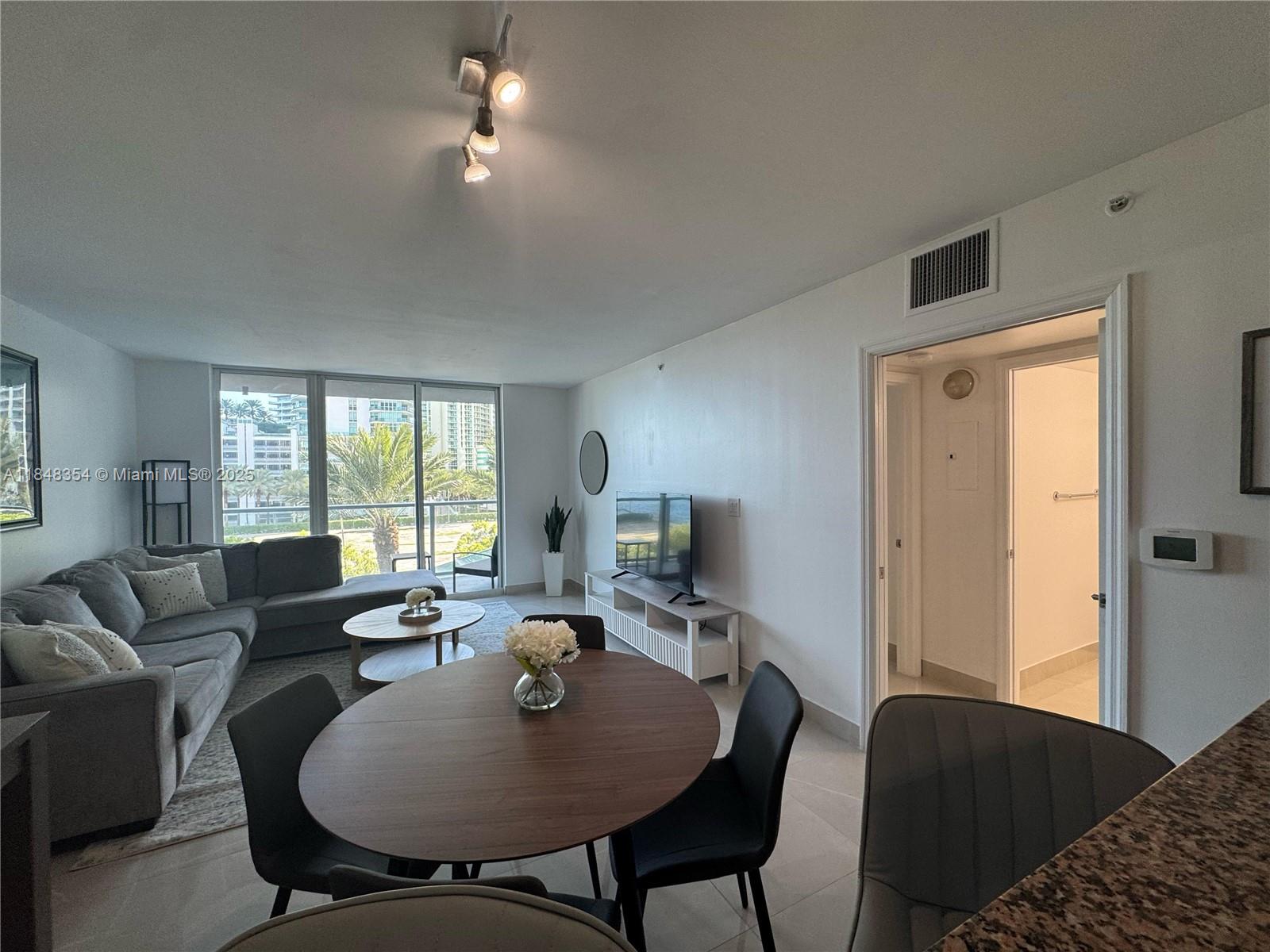 A living and dining area features a gray sectional sofa, round table, and balcony access — 1155 Brickell Bay Dr # 307, Miami FL 33131, MIAMI, FL