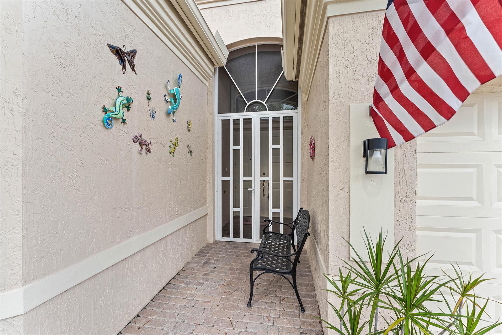 A paved entryway features a white storm door, a black metal bench, and wall decorations — 7188 Demedici Circle, Delray Beach FL 33446, DELRAY BEACH, FL
