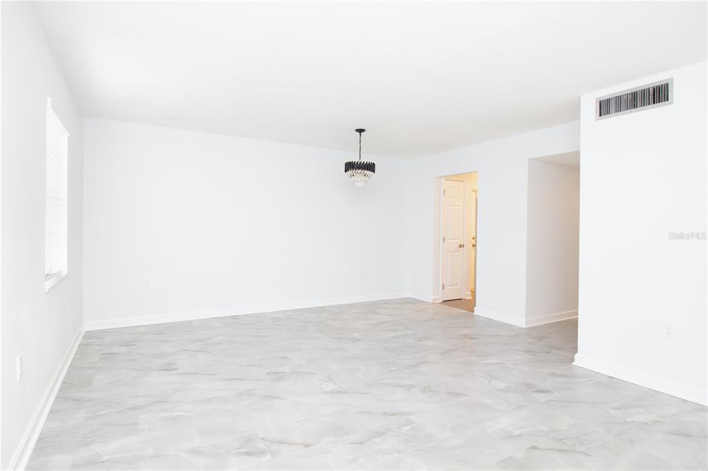 A bright, empty room features white walls, gray marble-look tile flooring, and a modern chandelier — 1115 RUE DES CHATEAUX UNIT 1A, SOUTH PASADENA, FL