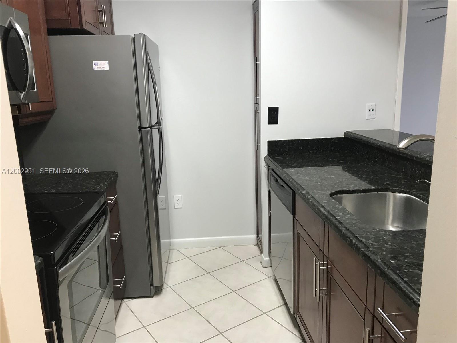 A kitchen features dark wood cabinets, stainless steel appliances, and black granite countertops — 7075 NW 186th St # C408, Hialeah FL 33015, HIALEAH, FL