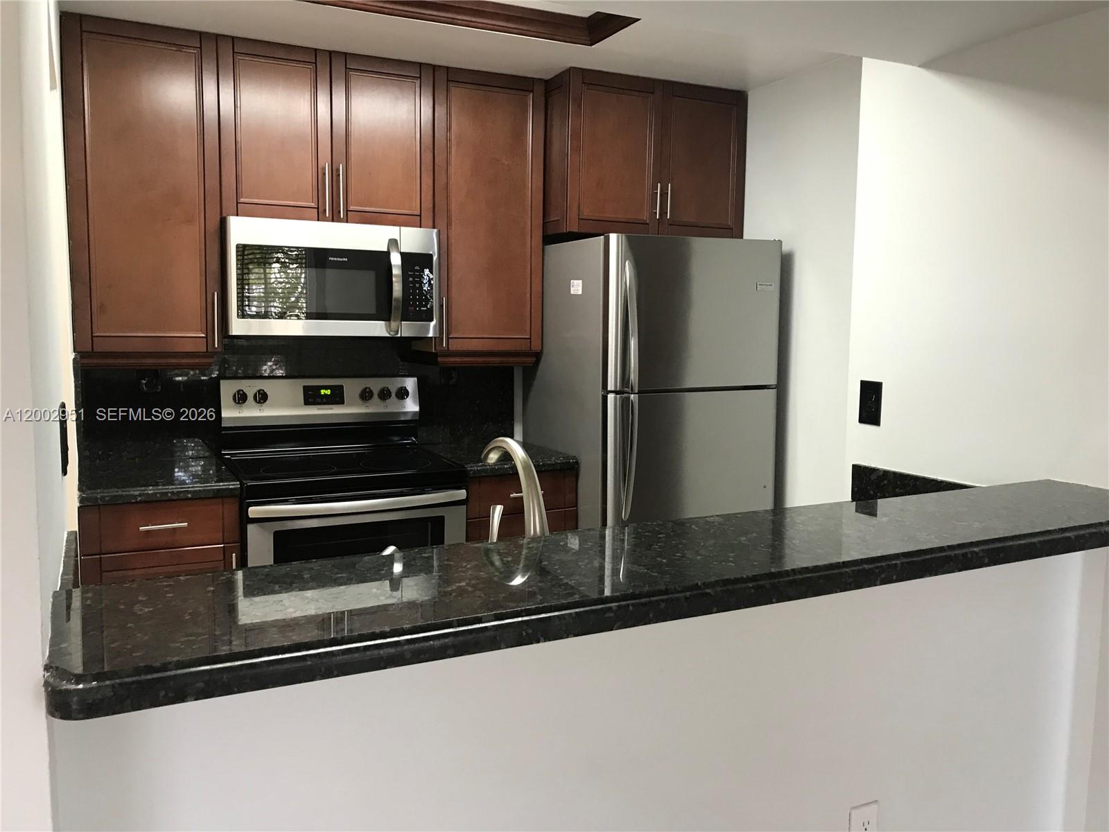 A kitchen features dark wood cabinets, stainless steel appliances, and a black granite countertop — 7075 NW 186th St # C408, Hialeah FL 33015, HIALEAH, FL