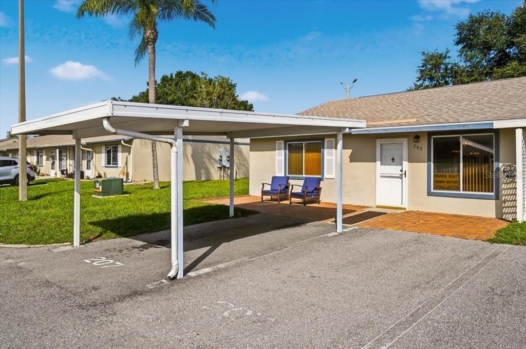 A single-story residential unit features a covered carport, a brick patio, and two blue chairs — 207 WINTER RIDGE BOULEVARD UNIT 4, WINTER HAVEN, FL