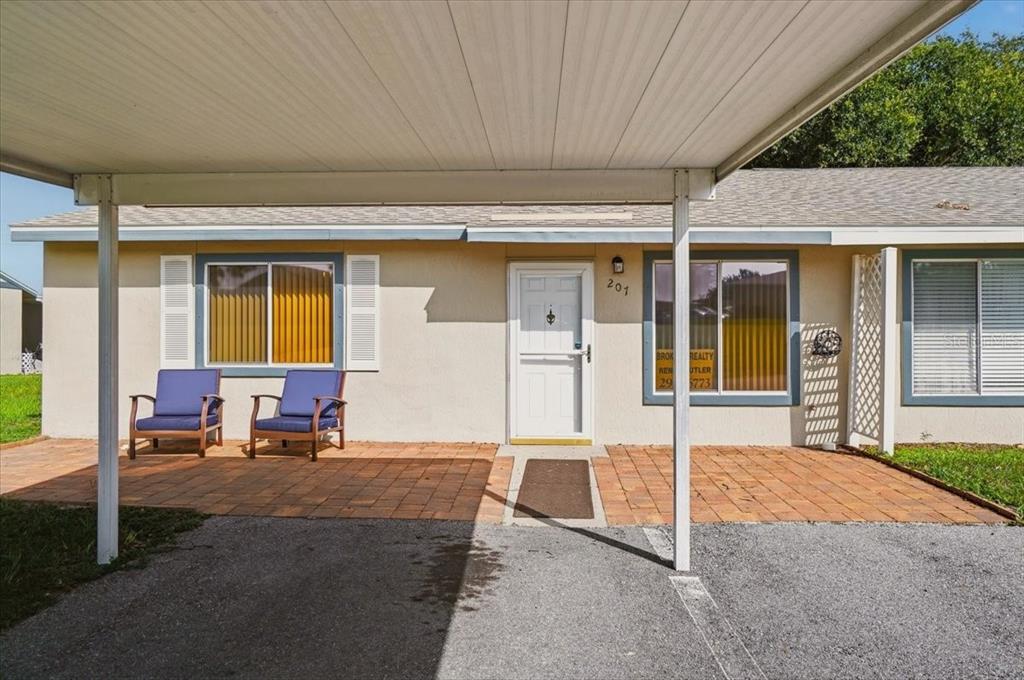 A single-story home exterior features a brick patio, a carport, and two blue chairs — 207 WINTER RIDGE BOULEVARD UNIT 4, WINTER HAVEN, FL