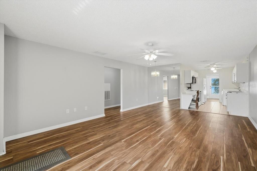 An open-concept living area with wood-look flooring, a ceiling fan, and an adjacent white kitchen — 207 WINTER RIDGE BOULEVARD UNIT 4, WINTER HAVEN, FL