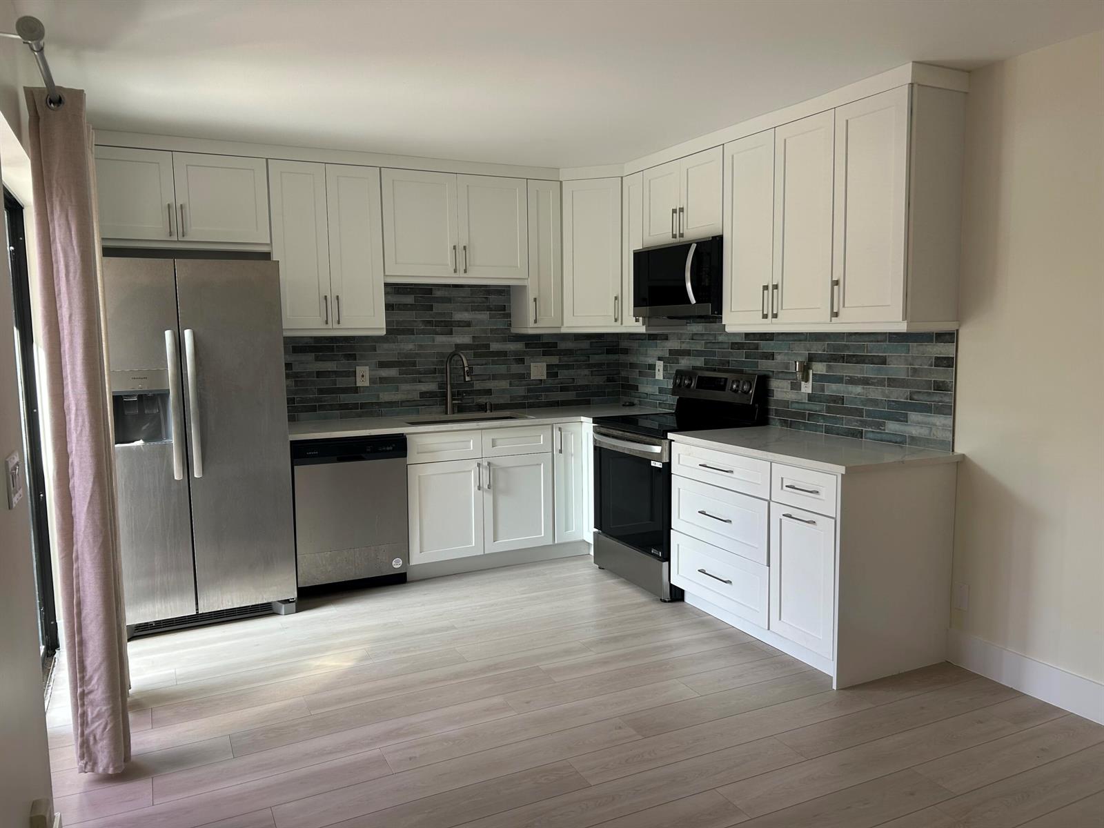 A kitchen with white cabinets, stainless steel appliances, and a blue-toned tiled backsplash — 2802 SW 12th Street, Deerfield Beach FL 33442, DEERFIELD BEACH, FL