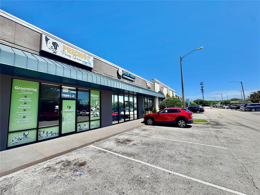 A red SUV is parked in front of a strip mall with a grooming salon — 3283 S JOHN YOUNG PARKWAY, KISSIMMEE, FL