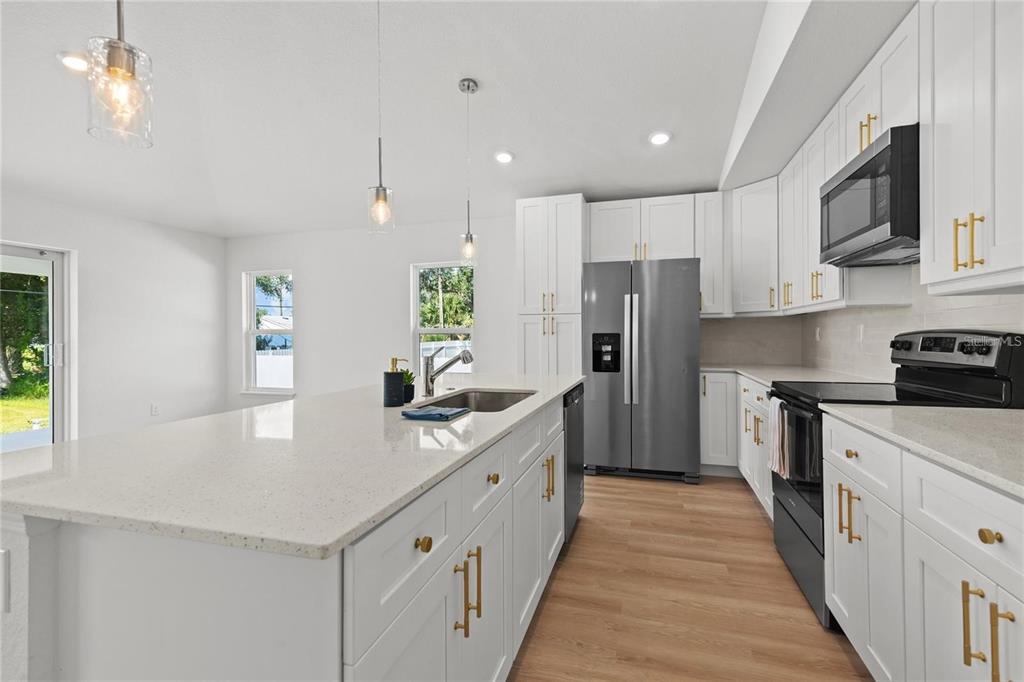 A modern kitchen features white cabinets, a quartz island, stainless steel appliances, and wood flooring — 4315 HUNGARY ROAD, NORTH PORT, FL