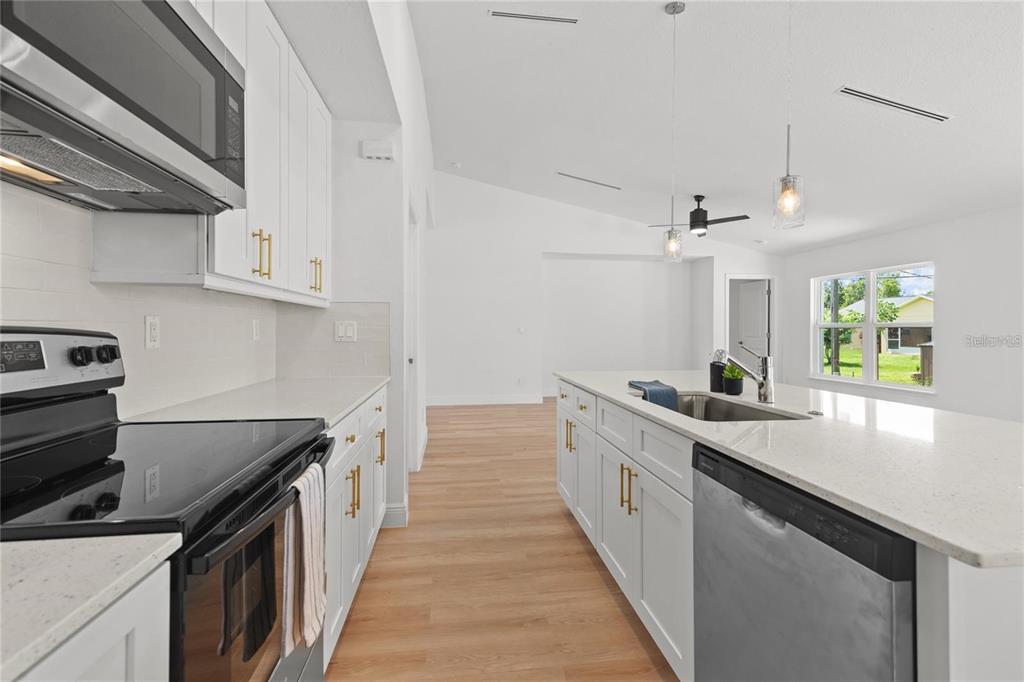 A modern kitchen features white cabinets, quartz countertops, stainless steel appliances, and light wood flooring — 4315 HUNGARY ROAD, NORTH PORT, FL