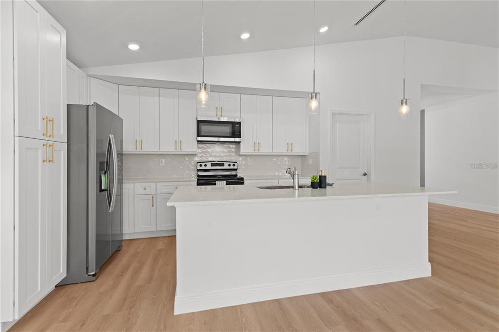 A modern kitchen features white cabinetry, stainless steel appliances, a center island, and wood flooring — 4315 HUNGARY ROAD, NORTH PORT, FL