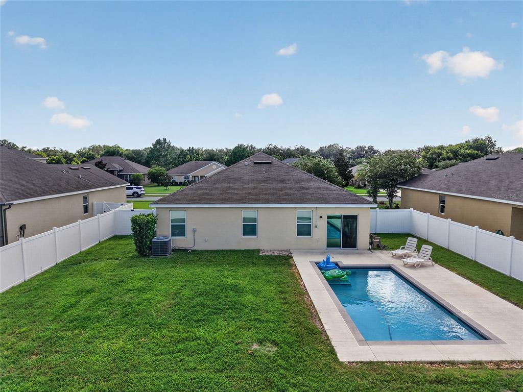 A backyard with a swimming pool, a grassy lawn, and a white vinyl privacy fence — 9785 PEPPER TREE TRAIL, WILDWOOD, FL