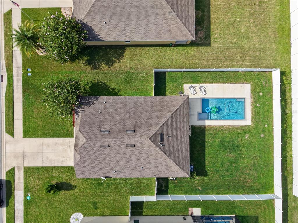An aerial view shows a house with a shingled roof, backyard pool, and fenced lawn — 9785 PEPPER TREE TRAIL, WILDWOOD, FL