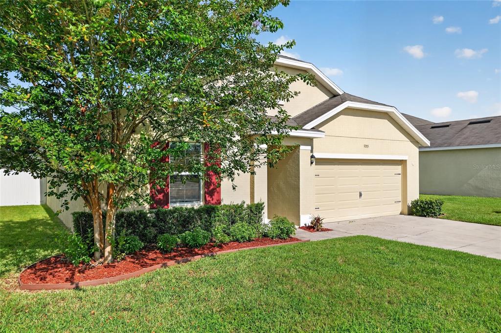 A beige single-story house with a two-car garage and a tree in the front yard — 9785 PEPPER TREE TRAIL, WILDWOOD, FL
