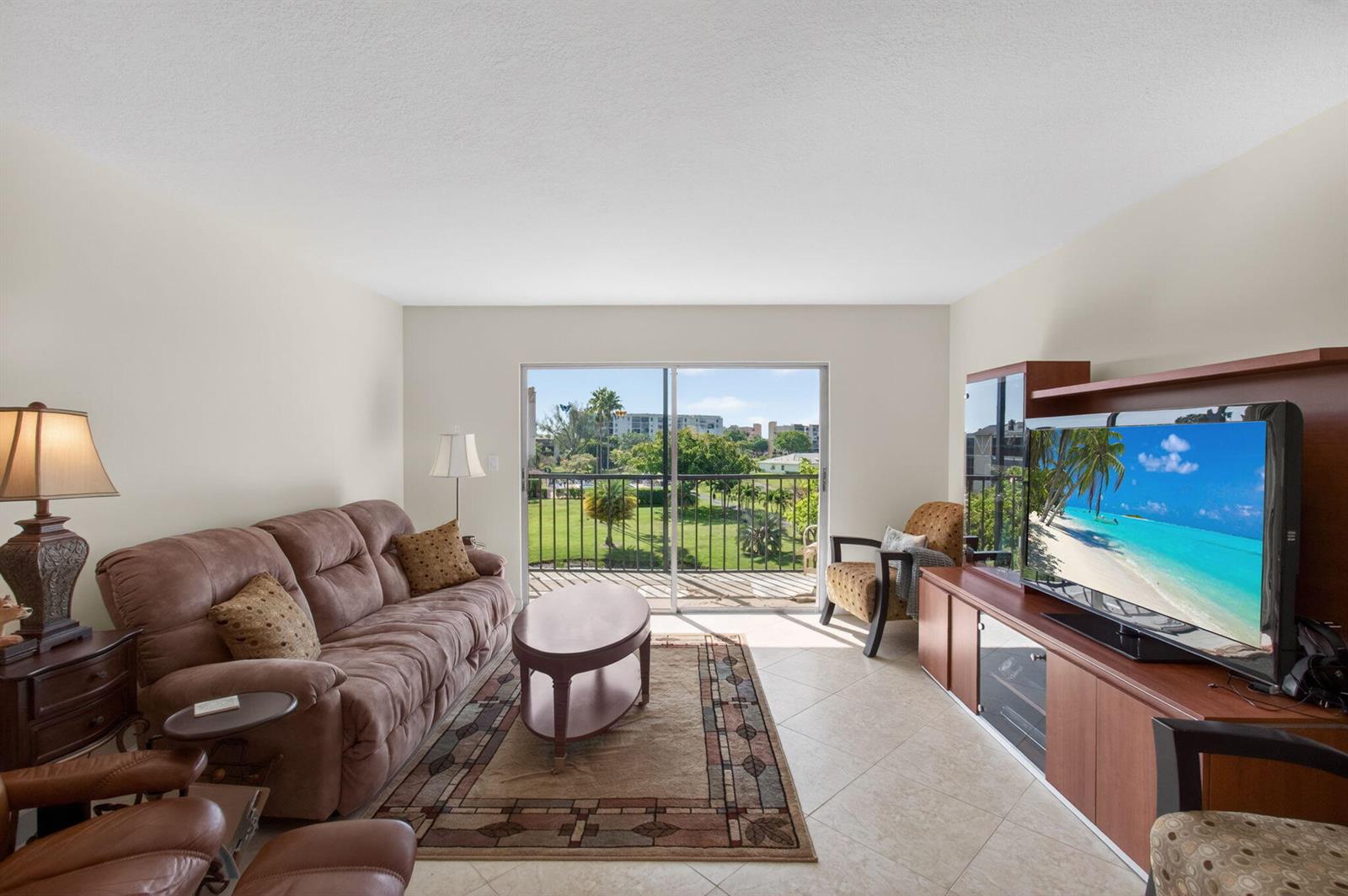A living room with a brown sofa, television console, and a balcony overlooking a lawn — 7006 Huntington Lane # 404, Delray Beach FL 33446, DELRAY BEACH, FL