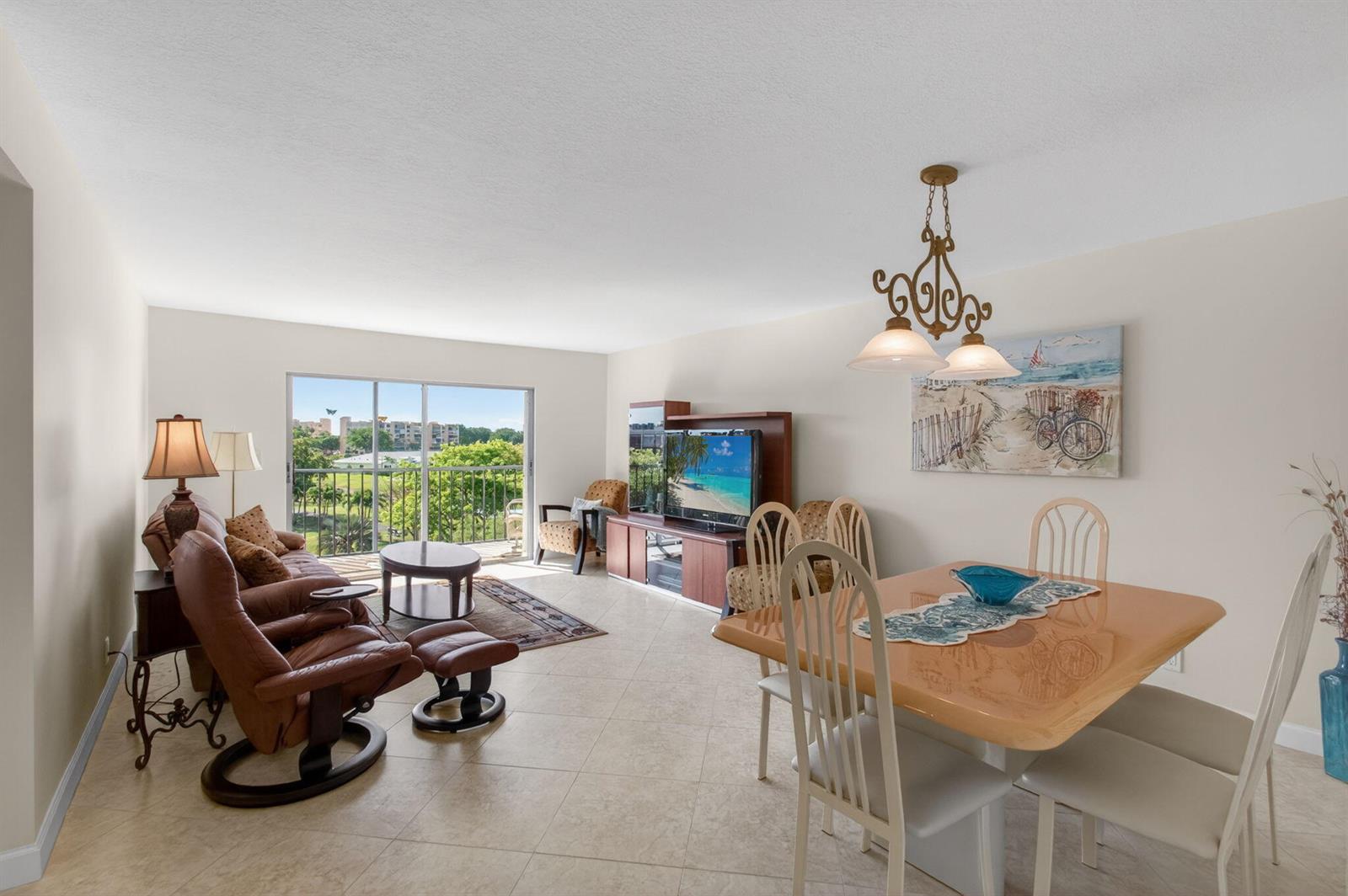 A living and dining area with tile floors, a leather recliner, and a balcony view — 7006 Huntington Lane # 404, Delray Beach FL 33446, DELRAY BEACH, FL