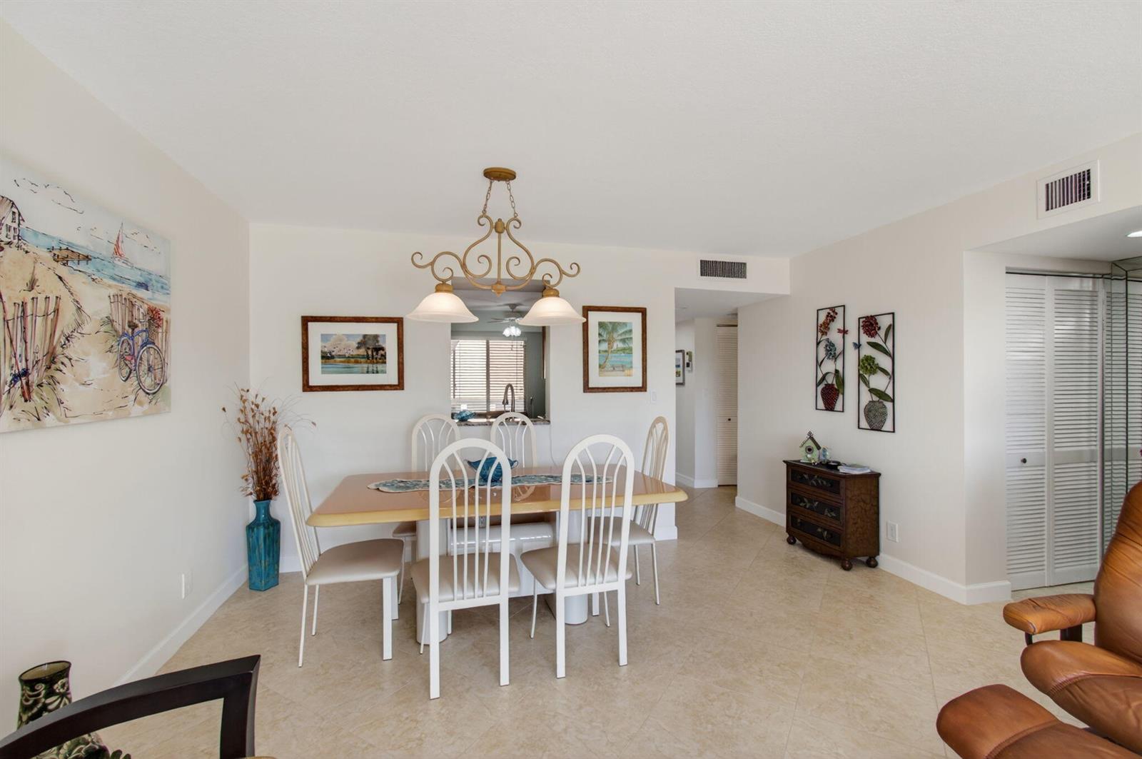 A dining area features a wooden table with white chairs, a chandelier, and tile flooring — 7006 Huntington Lane # 404, Delray Beach FL 33446, DELRAY BEACH, FL