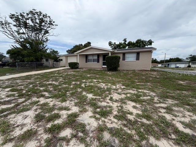 A single-story, light-colored brick house features a front-facing garage and a sparse, sandy lawn — 7539 GULF HIGHLANDS DRIVE, PORT RICHEY, FL