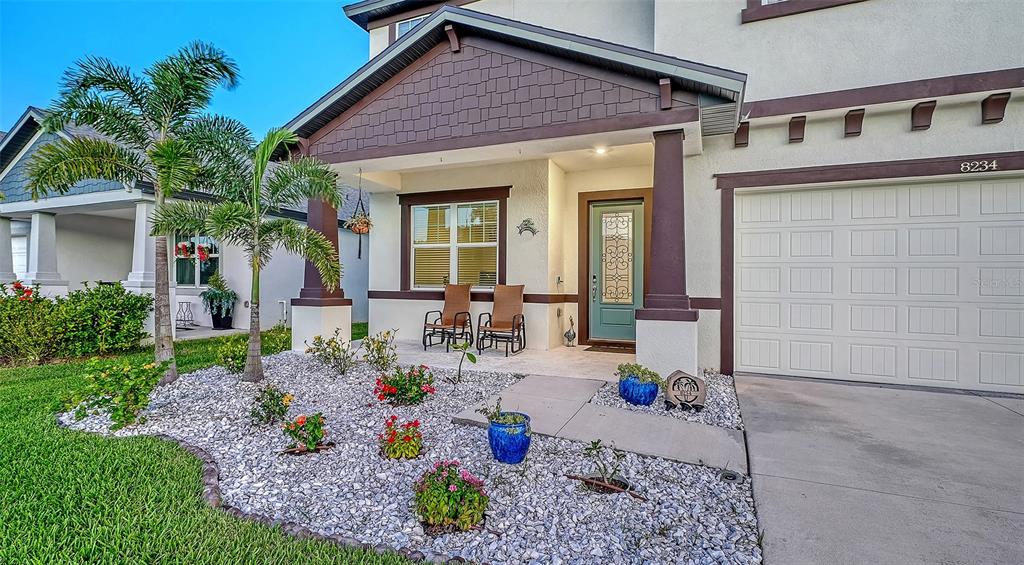 The exterior of a house features a covered porch, a garage, and a landscaped yard — 8234 TEA OLIVE TERRACE, PALMETTO, FL