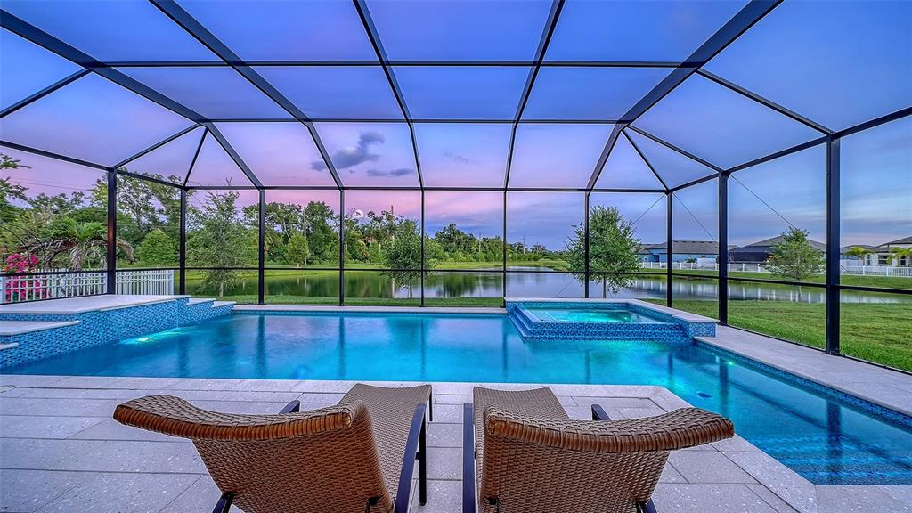 A screened-in swimming pool and spa overlook a pond at dusk — 8234 TEA OLIVE TERRACE, PALMETTO, FL