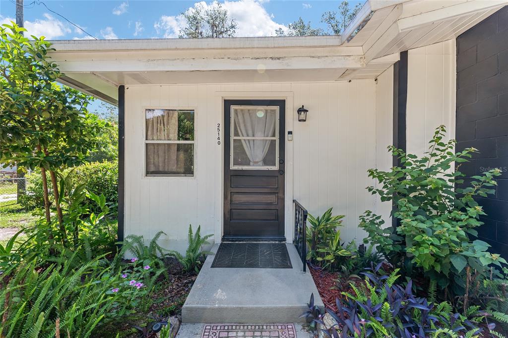 A front exterior view of a house entrance with a dark door and white siding — 25140 NE 133RD PLACE, SALT SPRINGS, FL