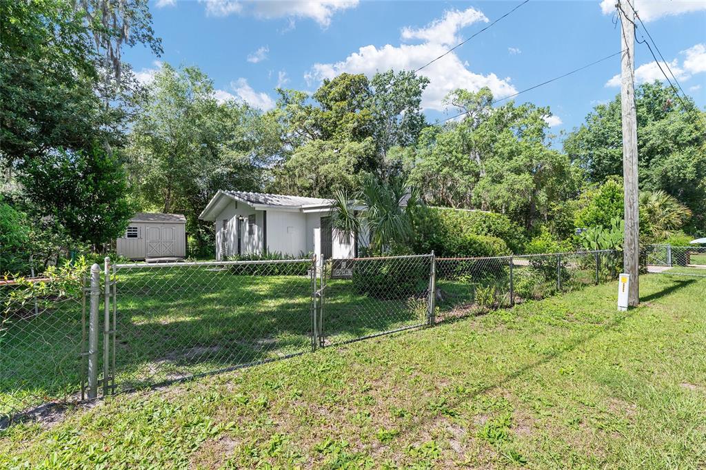 A white single-story house sits behind a chain-link fence with a shed in the yard — 25140 NE 133RD PLACE, SALT SPRINGS, FL