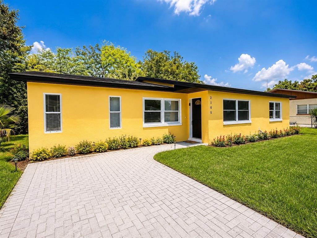 A yellow single-story house features a paved driveway, a black roof, and a front lawn — 2105 9TH STREET NE, WINTER HAVEN, FL