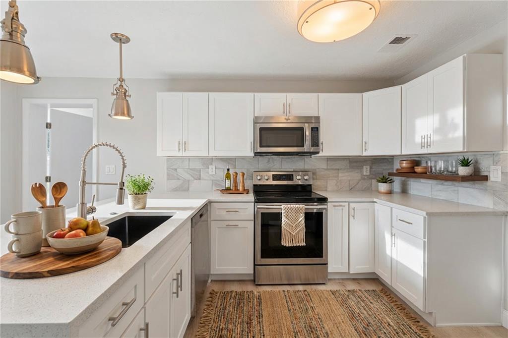 A modern kitchen features white cabinets, stainless steel appliances, quartz countertops, and a tile backsplash — 2105 9TH STREET NE, WINTER HAVEN, FL