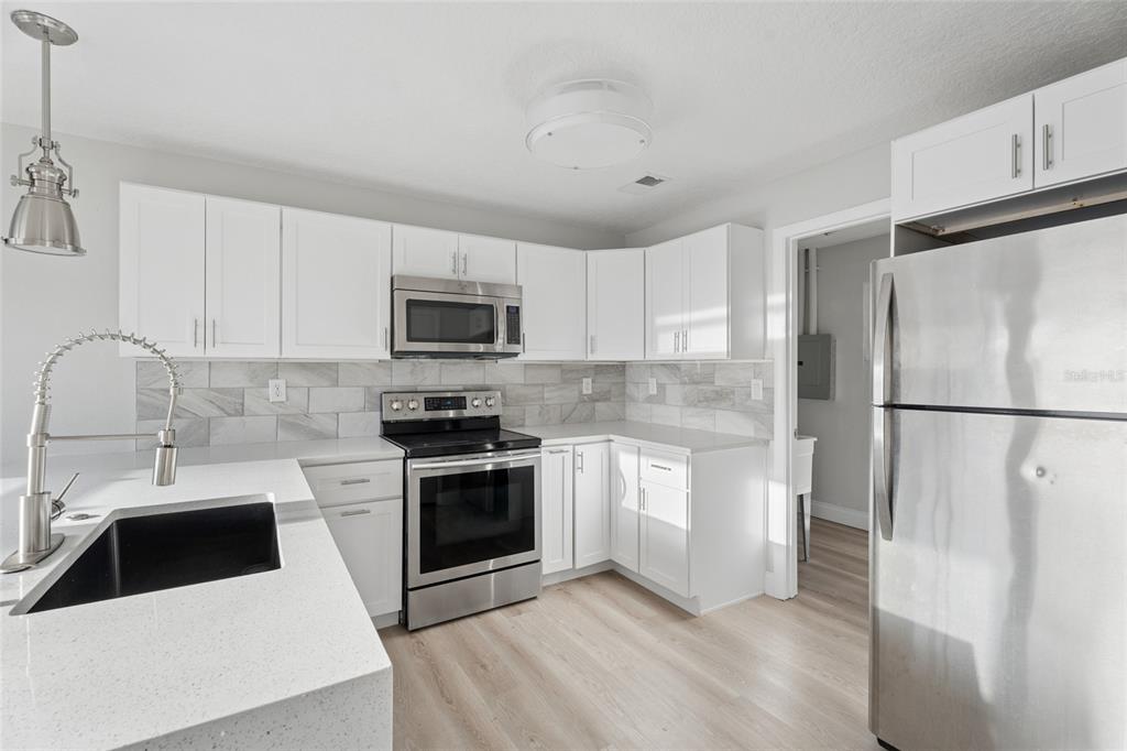 A modern kitchen features white cabinetry, stainless steel appliances, a quartz countertop, and tile backsplash — 2105 9TH STREET NE, WINTER HAVEN, FL