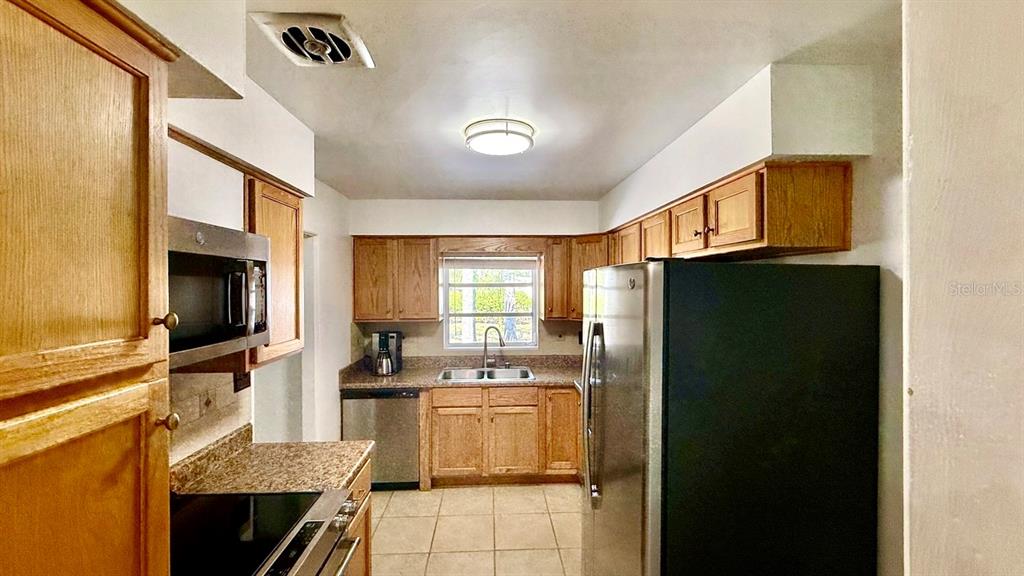A kitchen features wood cabinets, stainless steel appliances, granite countertops, and light-colored tile flooring — 716 50TH STREET COURT W, BRADENTON, FL