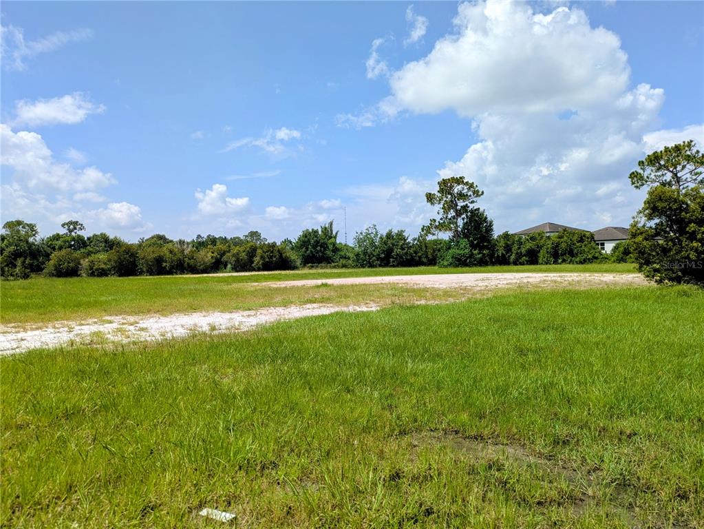 A grassy, vacant lot features a dirt path under a blue sky with clouds — CORD AVENUE, ST CLOUD, FL