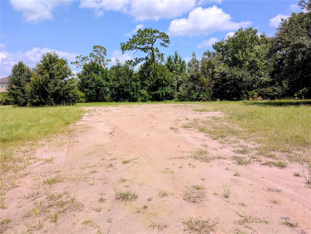 A sandy, unpaved lot is surrounded by green trees under a blue sky — CORD AVENUE, ST CLOUD, FL