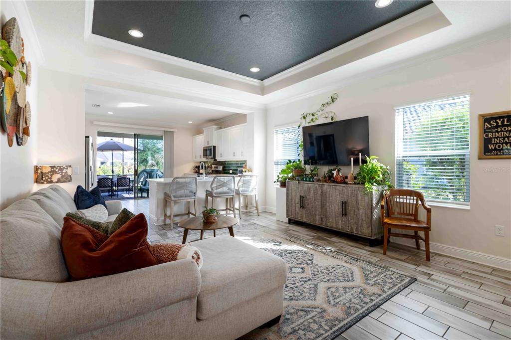A living room with a tray ceiling, sectional sofa, and an open kitchen in the background — 2669 STAR APPLE WAY, SARASOTA, FL