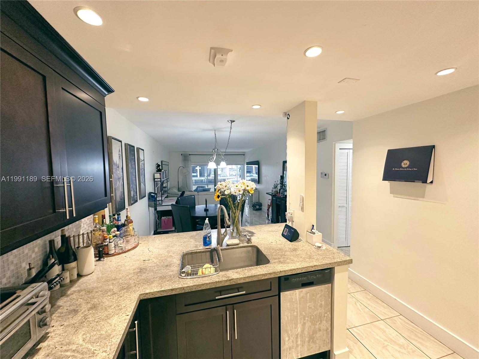 A kitchen with dark cabinets and granite countertops overlooks a dining and living area — 450 Paradise Isle Blvd # 102, Hallandale Beach FL 33009, HALLANDALE BEACH, FL