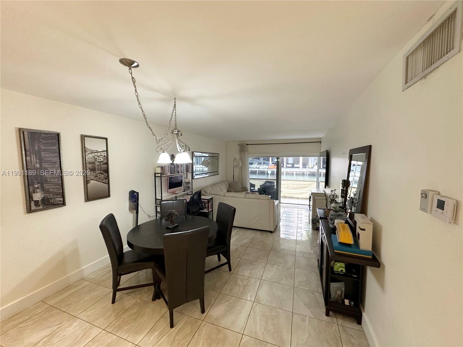 A dining area and living room with tile floors overlook a canal through sliding doors — 450 Paradise Isle Blvd # 102, Hallandale Beach FL 33009, HALLANDALE BEACH, FL