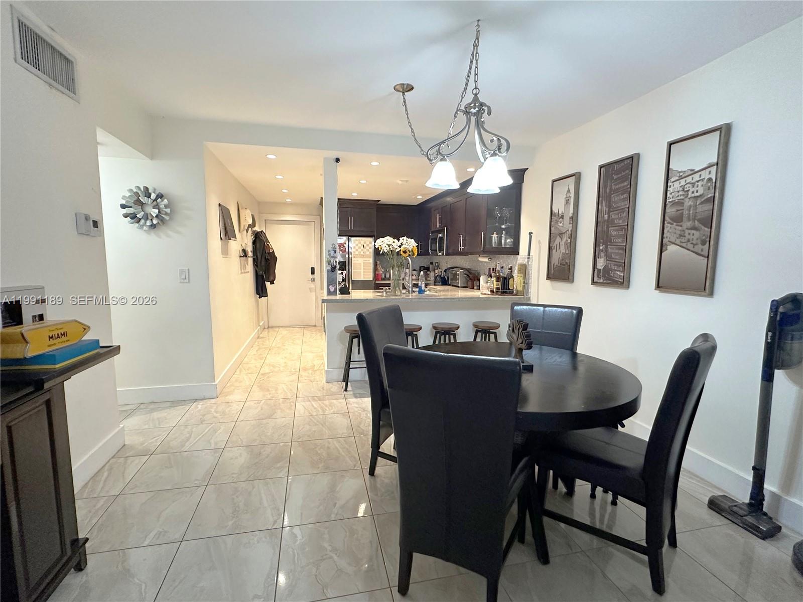 A dining area with a round table and chairs sits adjacent to an open kitchen — 450 Paradise Isle Blvd # 102, Hallandale Beach FL 33009, HALLANDALE BEACH, FL